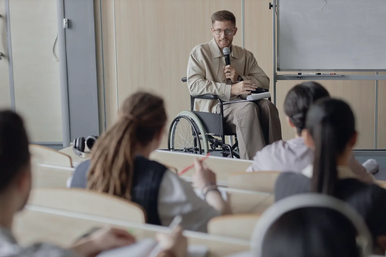 Teacher who uses a wheelchair speaking with a microphone to a seated classroom audience