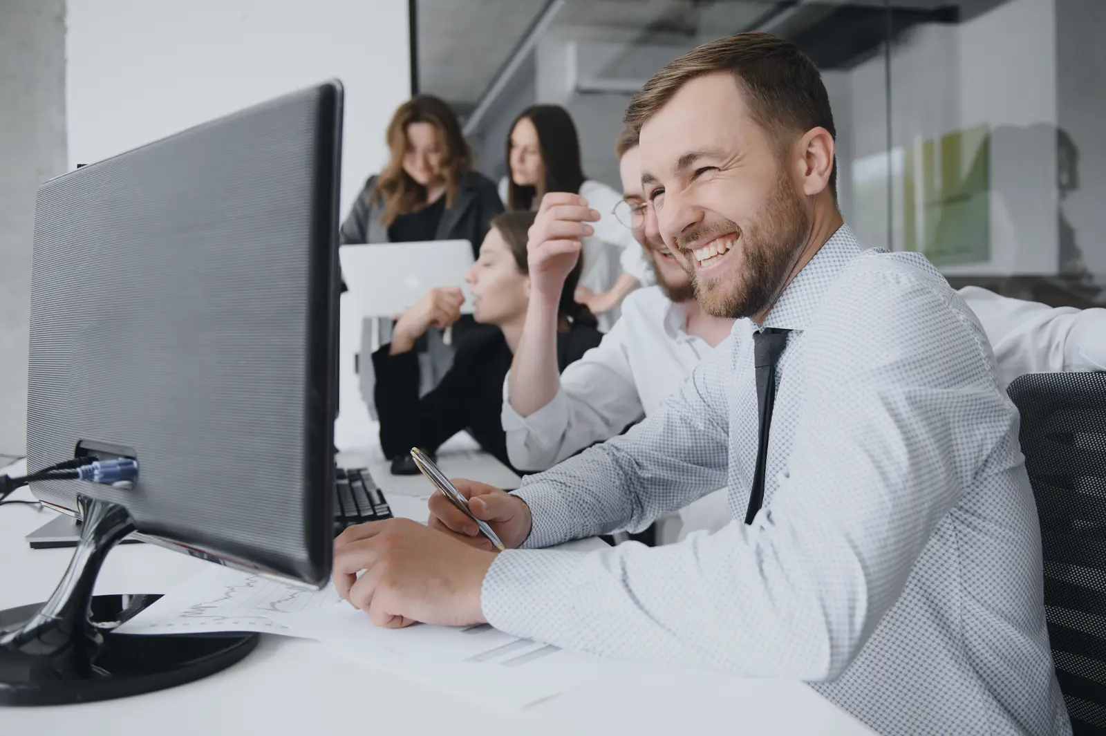 Smiling team member collaborating with colleagues at his desk in a modern office